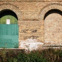 An arched turquoise door and bricked in window with graffiti writing on the wall between them.